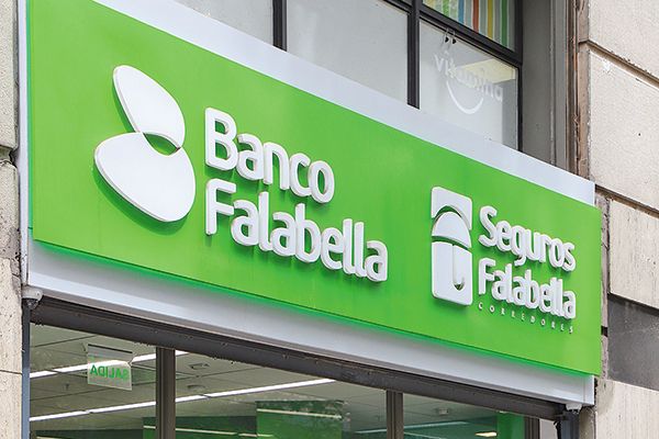 Persona adulta revisando documentos de cobertura médica junto a un ejecutivo de seguros en una oficina con logo de Falabella visible al fondo