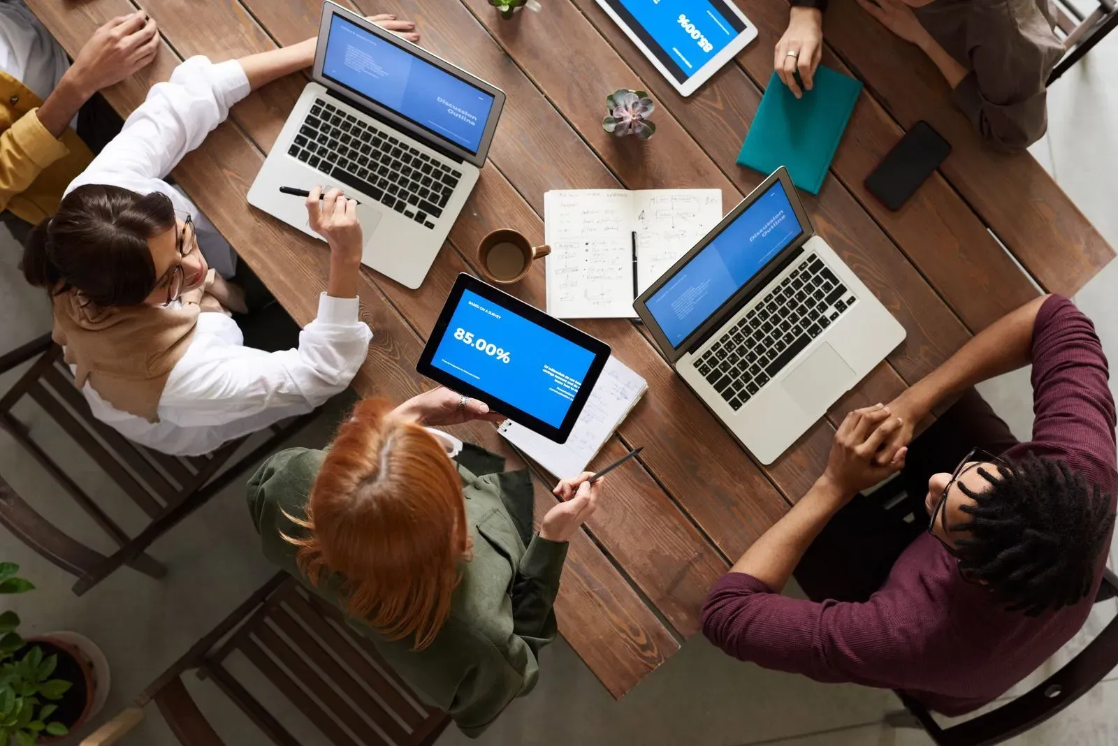 Equipo de trabajo revisando datos y planillas en laptops y tablets alrededor de una mesa
